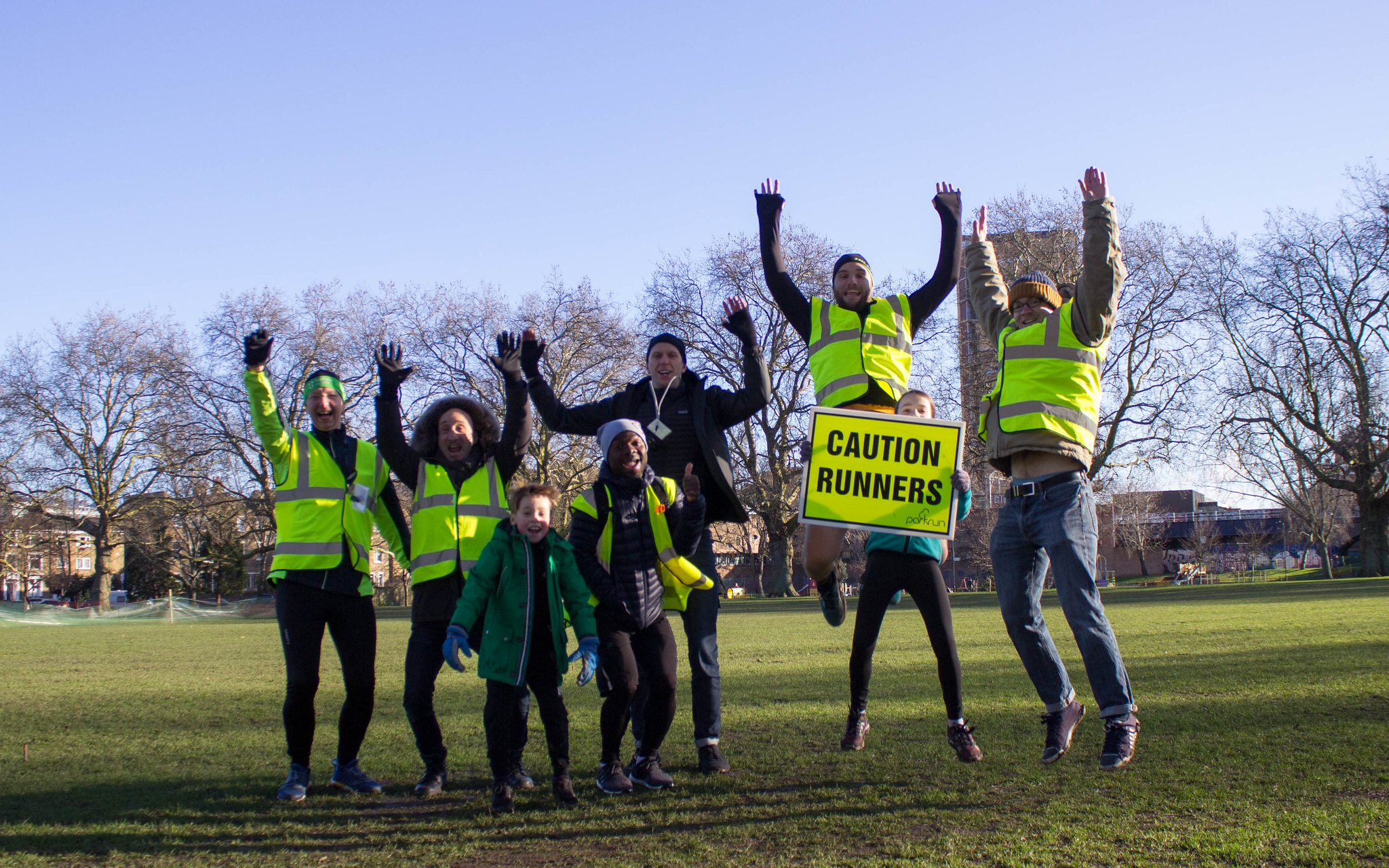 Group of volunteers in fluorescent vests jumping in the air in a park