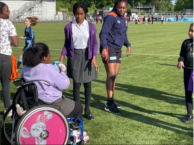 Young Black girl in wheelchair catches a ball in a park, playing with girl in uniform and girl in sports kit
