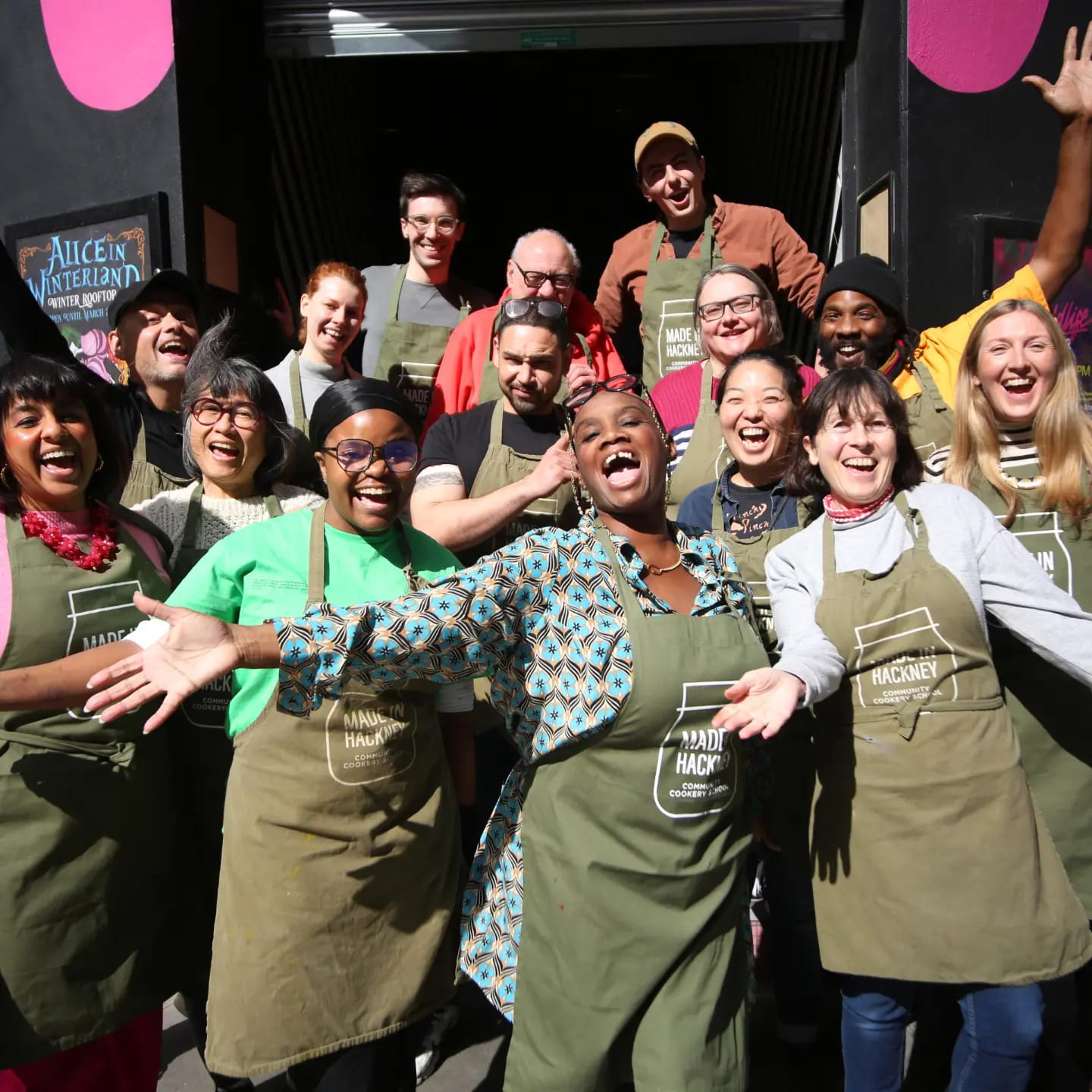 Diverse group of volunteers in Made in Hackney aprons cheering and laughing