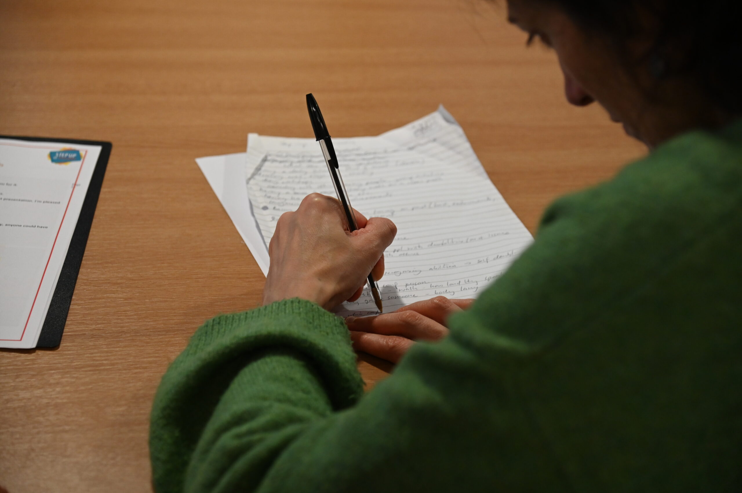 close up of person in green jumper writing